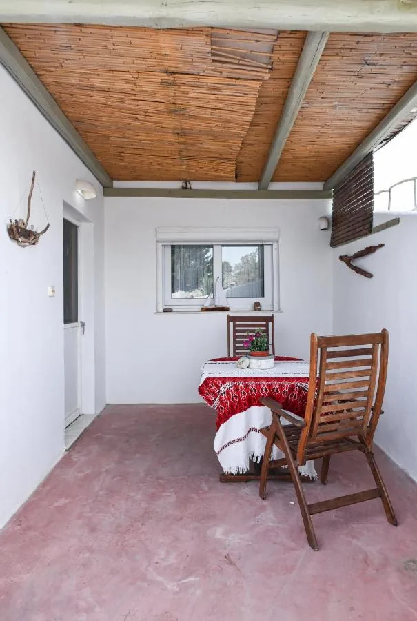 The patio of Navis Apartment under a cane roof, with a wooden chair and a red cushion